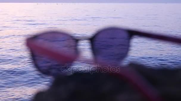 Modieuze zonnebrillen liggen op steen op de achtergrond van de zee — Stockvideo