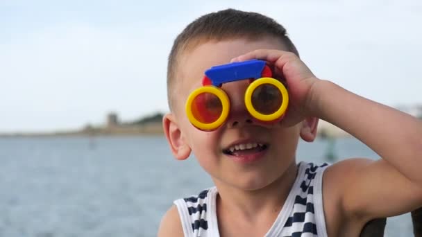 Divertido niño con camisa a rayas mirando a través de los prismáticos en la cámara — Vídeos de Stock