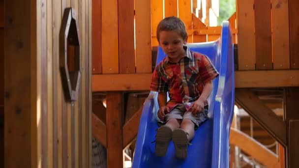 Liten pojke i en rutig skjorta rullar nedför backen — Stockvideo