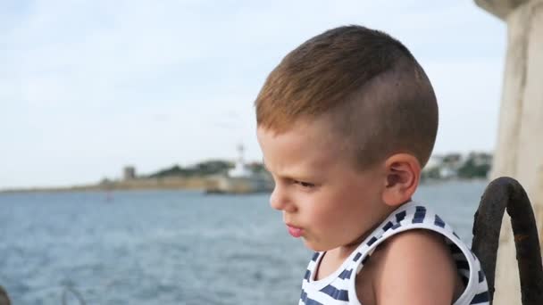 Говорящий маленький мальчик в матросских полосах рубашку на небе и на фоне моря — стоковое видео