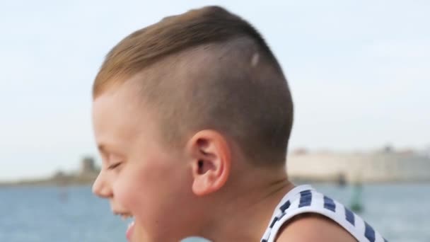 Niño sonriente y riendo en franjas marineras camiseta sin mangas en el cielo y el fondo del mar — Vídeos de Stock