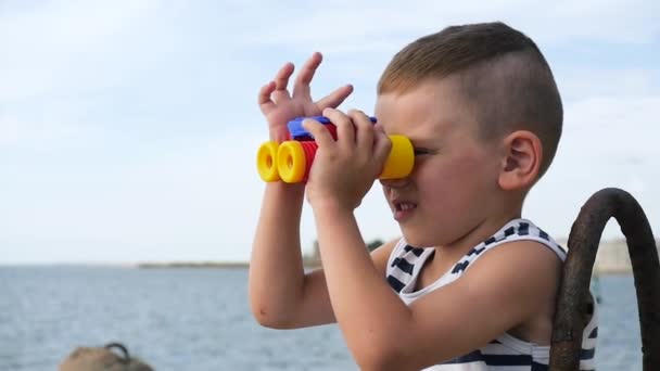Красивый маленький ребенок играет с игрушечным биноклем на фоне неба — стоковое видео