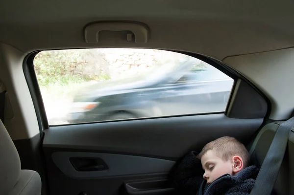 Petit garçon dormir à l'intérieur de la voiture près de la fenêtre avec voiture de passage derrière — Photo