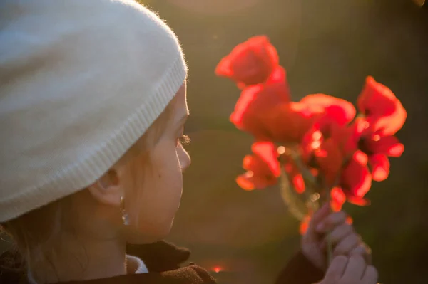 Little girl wearing hat holding bouquet of poppy flowers in spring sunset — Stock Photo, Image
