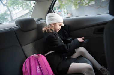 little girl in coat and hat sitting with a backpack in the car clipart