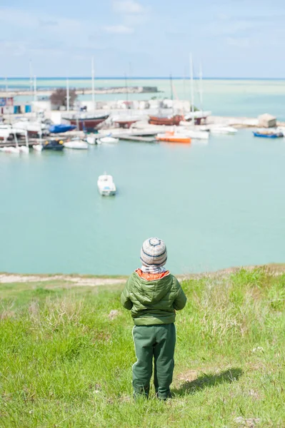 Piccolo ragazzo in giacca e cappello guarda il molo del mare in primavera — Foto Stock