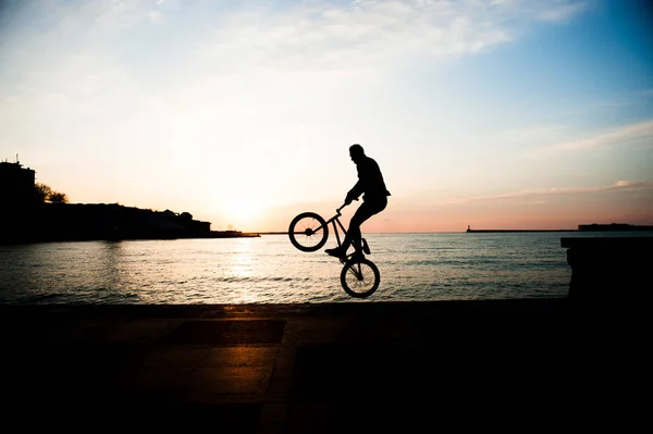 Jonge man springen met de fiets op de achtergrond van de zee in de stad in de zonsondergang — Stockfoto