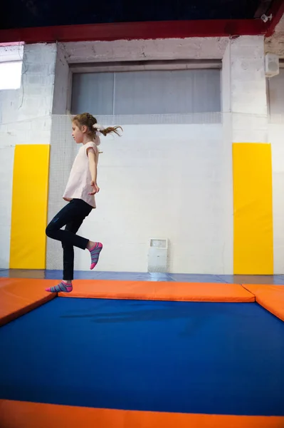 Sottile bambina saltando su trampolino coperto — Foto Stock