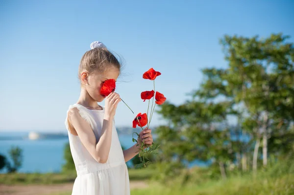 Slim little girl sniffing red flowers outdoors near sea in spring — Stock Photo, Image