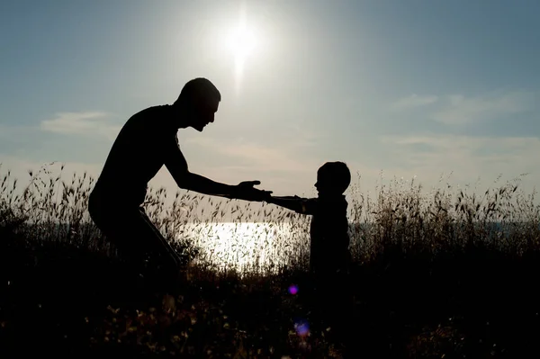 Ojciec i syn trzymać się za ręce i spojrzeć na siebie na tle zachodu słońca nad morzem — Zdjęcie stockowe