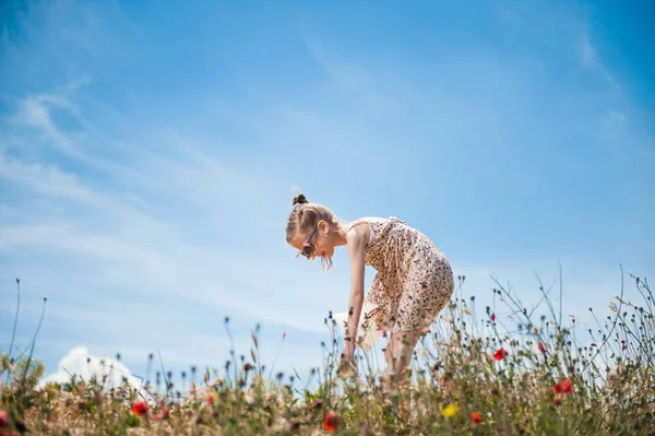 Bonito menina no vestido dobrado para baixo para escolher flores no campo — Fotografia de Stock