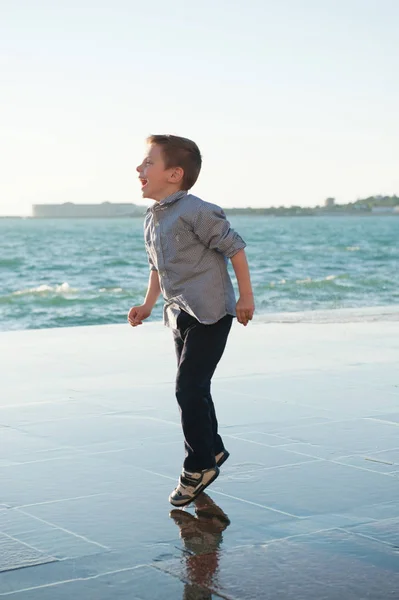 Glad söt pojke står mot havet i staden ropade — Stockfoto