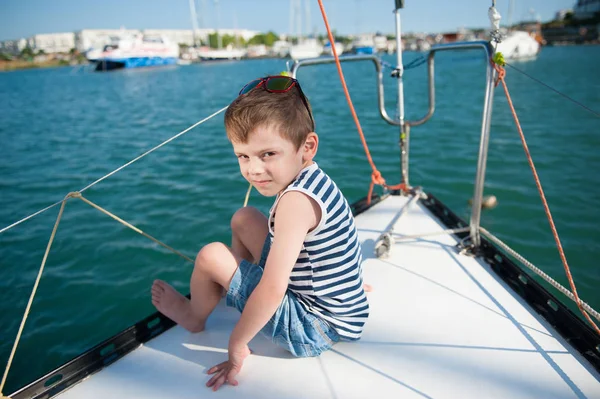 可爱的小男孩短裤和条纹 t恤坐在船上的海港游艇在海港 — 图库照片
