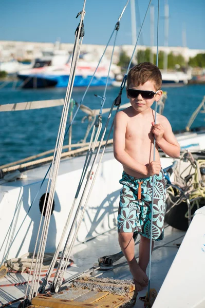 Carino bambino in pantaloncini e occhiali da sole a bordo di uno yacht in estate — Foto Stock