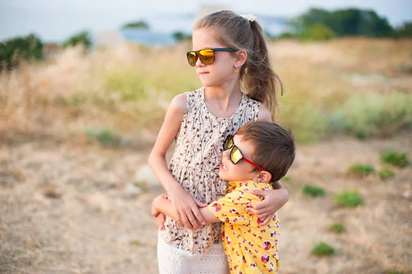 Bonito menina e menino vestindo óculos de sol abraçando no campo no verão — Fotografia de Stock