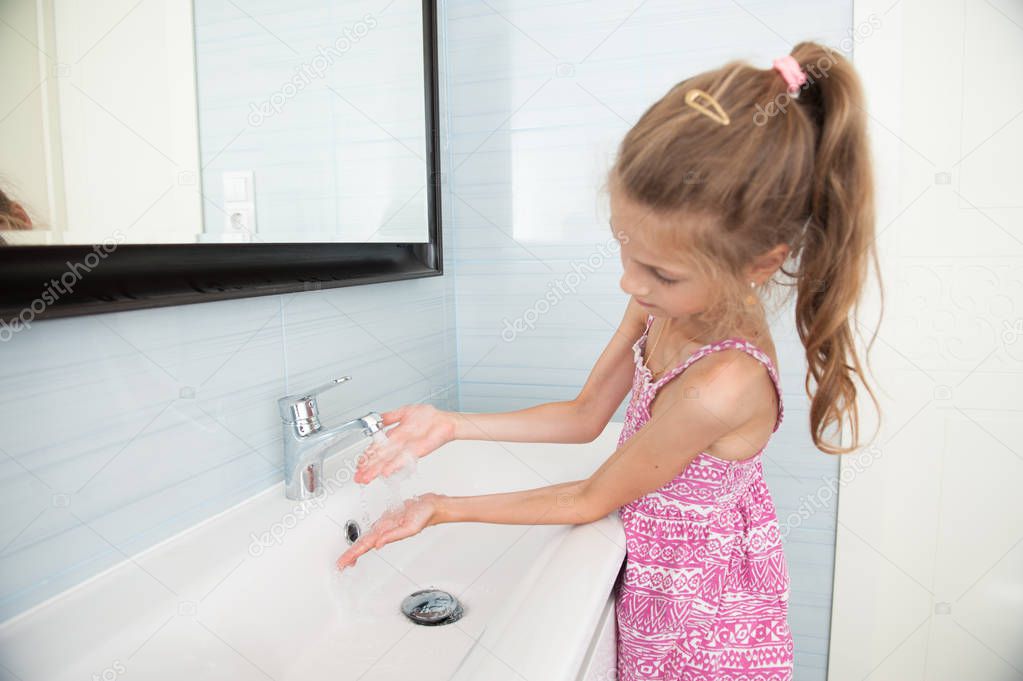 cute little girl in dress washes her hands in washbasin in bright bathroom