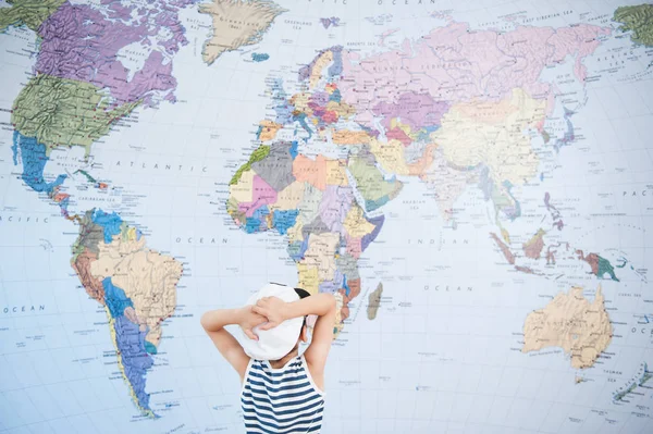 Little boy in the hat of captain looking at world map, clutching his head — Stock Photo, Image
