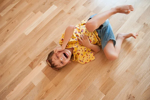 Grappige schattige kleine jongen in shirt en broek ligt op vloer en lacht — Stockfoto