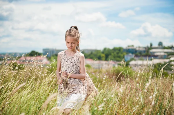 Carina bambina passa attraverso un campo con un cielo blu su uno sfondo in primavera — Foto Stock