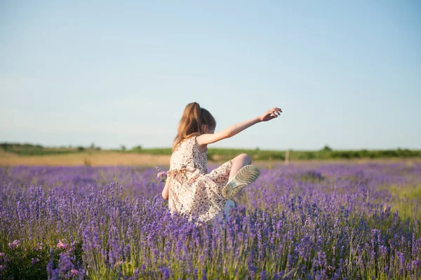 Menina engraçada fina no vestido cruza arbustos altos no campo entre flores de lavanda — Fotografia de Stock