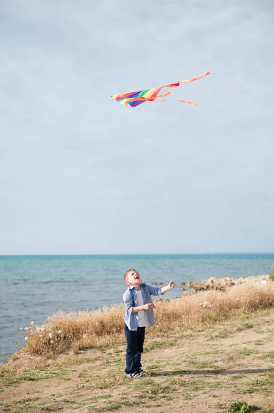 Carino bambino tiene aquilone colorato volare nel cielo blu vicino alla costa del mare in estate — Foto Stock