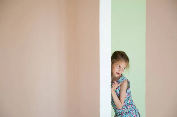Beautiful small smiling girl hid behind the corner in new room — Stock Photo, Image