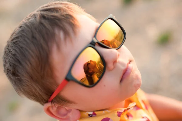 Милый маленький мальчик в солнечных очках, которые отражают красивую маленькую девочку в летний вечер — стоковое фото