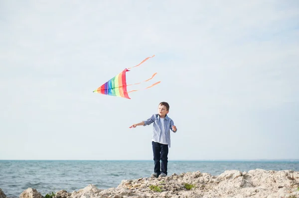 Felice bambino piccolo gioca con aquilone colorato sullo sfondo del mare e del cielo con spazio copia — Foto Stock