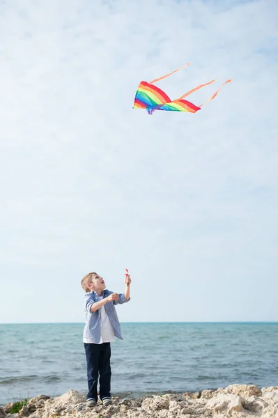 Bella caucasico bambino indossa camicia giocando aquilone volante dalla riva del mare — Foto Stock