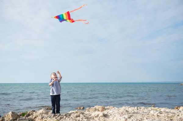 Χαριτωμένο μικρό αγόρι εκμετάλλευση kite διογκούμενων στον ουρανό φόντο ανοικτής θαλάσσης — Φωτογραφία Αρχείου