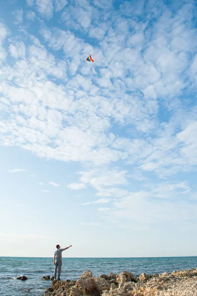 Υγιής νεαρός άνδρας εκμετάλλευση πολύχρωμο χαρταετό σε σχοινί εναντίον μπλε ουρανού και θάλασσας — Φωτογραφία Αρχείου