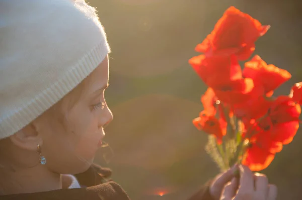 Hermosa niña pequeña con ramo de amapolas en sus manos iluminadas por la cálida luz del atardecer a principios de primavera —  Fotos de Stock