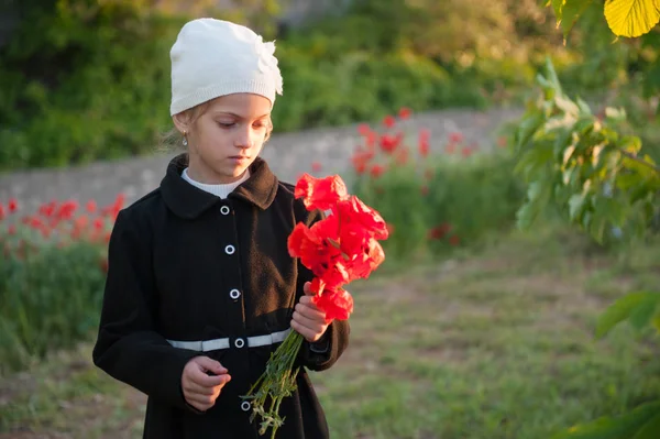 Triste menina bonita em chapéu e casaco com buquê de papoilas em uma mão no pôr do sol da primavera — Fotografia de Stock