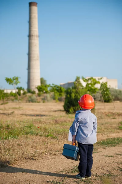 Piccolo bambino in età prescolare casco con scatola di strumenti di lavoro in mano guarda il tubo di scarico del vecchio impianto — Foto Stock