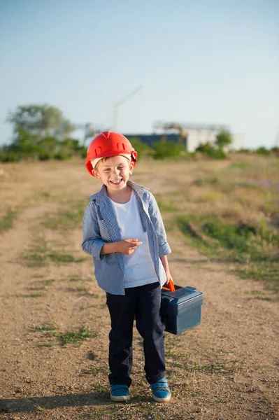 Щасливий усміхнений маленький хлопчик в шоломі з інструментами йде на роботу в літній день — стокове фото