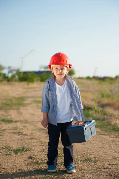 Смешной маленький милый ребенок в оранжевом шлеме с коробкой инструментов идет на работу — стоковое фото