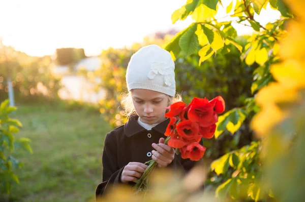 Niña pensativa en sombrero y abrigo sosteniendo ramo de flores de amapola roja en primavera —  Fotos de Stock