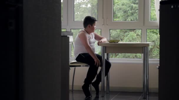 脂肪の食卓 台所に座っている少年は ウィンドウの背景にスープを食べる — ストック動画