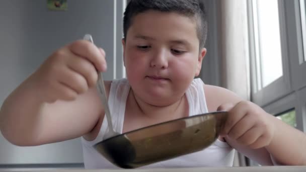 肖像画の問題小児肥満症のスープのスプーンを食べるキッチンで座っている魅力的な少し太った少年 — ストック動画