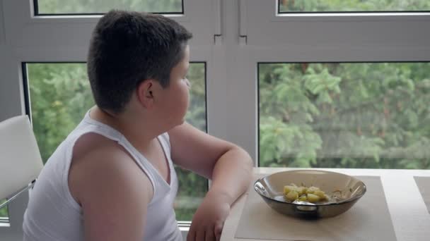 座って少し太った少年は付近のウィンドウとおいしいスープを食べる 小児肥満の概念 — ストック動画