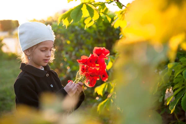 Menina bonita em chapéu e casaco segurando buquê de flores de papoula vermelha na primavera — Fotografia de Stock