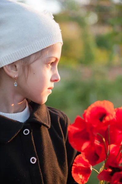 Ritratto di graziosa bambina in cappello bianco e cappotto nero con mazzo di fiori di papavero rosso in primavera sera — Foto Stock