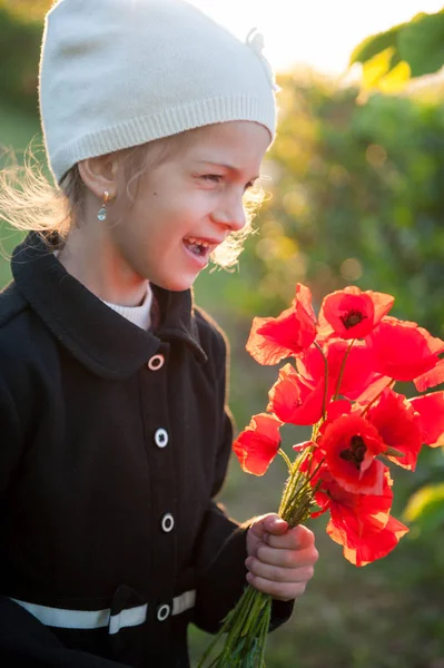 Heureux drôle petite fille caucasienne en chapeau et manteau avec bouquet de coquelicots dans ses mains au printemps — Photo