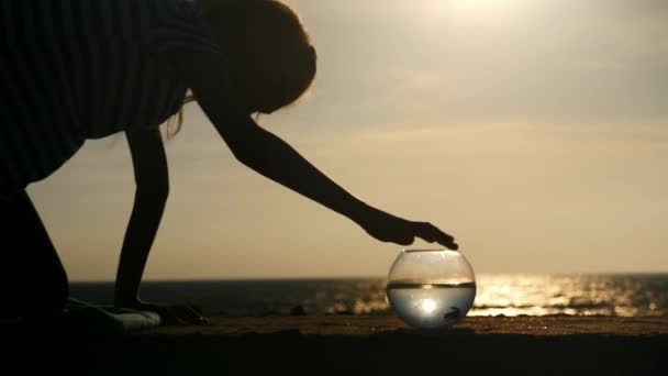 剪影小女孩玩她的宠物金鱼在水族馆海滨日落 — 图库视频影像