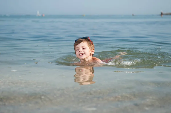 Felice sorridente carino bambino in occhiali da sole nuotare in acqua di mare in estate giornata di sole vacanza godendo — Foto Stock