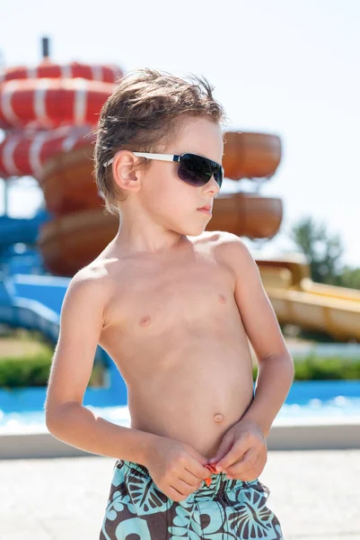 Duro ragazzo sano caucasico carino in pantaloncini e occhiali da sole nel parco acquatico in giorno di sole estivo — Foto Stock