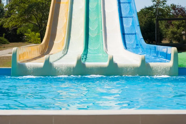 Water park with colorful water slides and blue swimming pool in summer sunny day