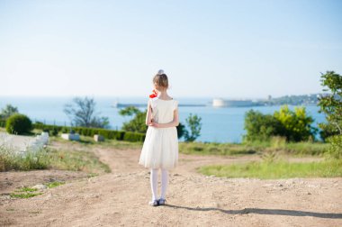 lonely thin little girl in white dress holding bouquet of red poppy standing on sea bay background clipart