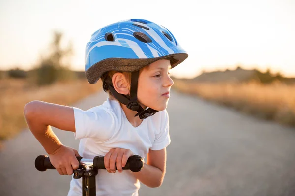 Staand of schattig klein kind in de sport helm staande op de verlaten weg in Texas met scooter in de warme zomer zonsondergang — Stockfoto
