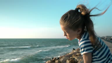 Dalgalar yavaş hareket sevimli küçük kız sahilde oturuyor görünüyor.